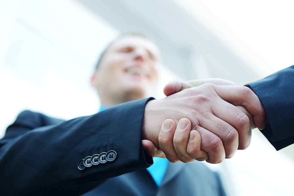 Business shaking hands in front of modern building with copy space (selective focus)